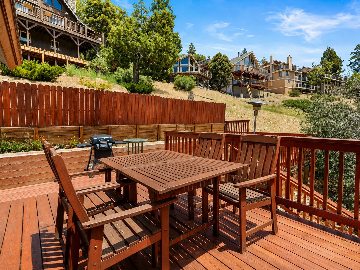 Una terraza de madera con mesa y sillas, rodeada por una valla de madera y árboles.