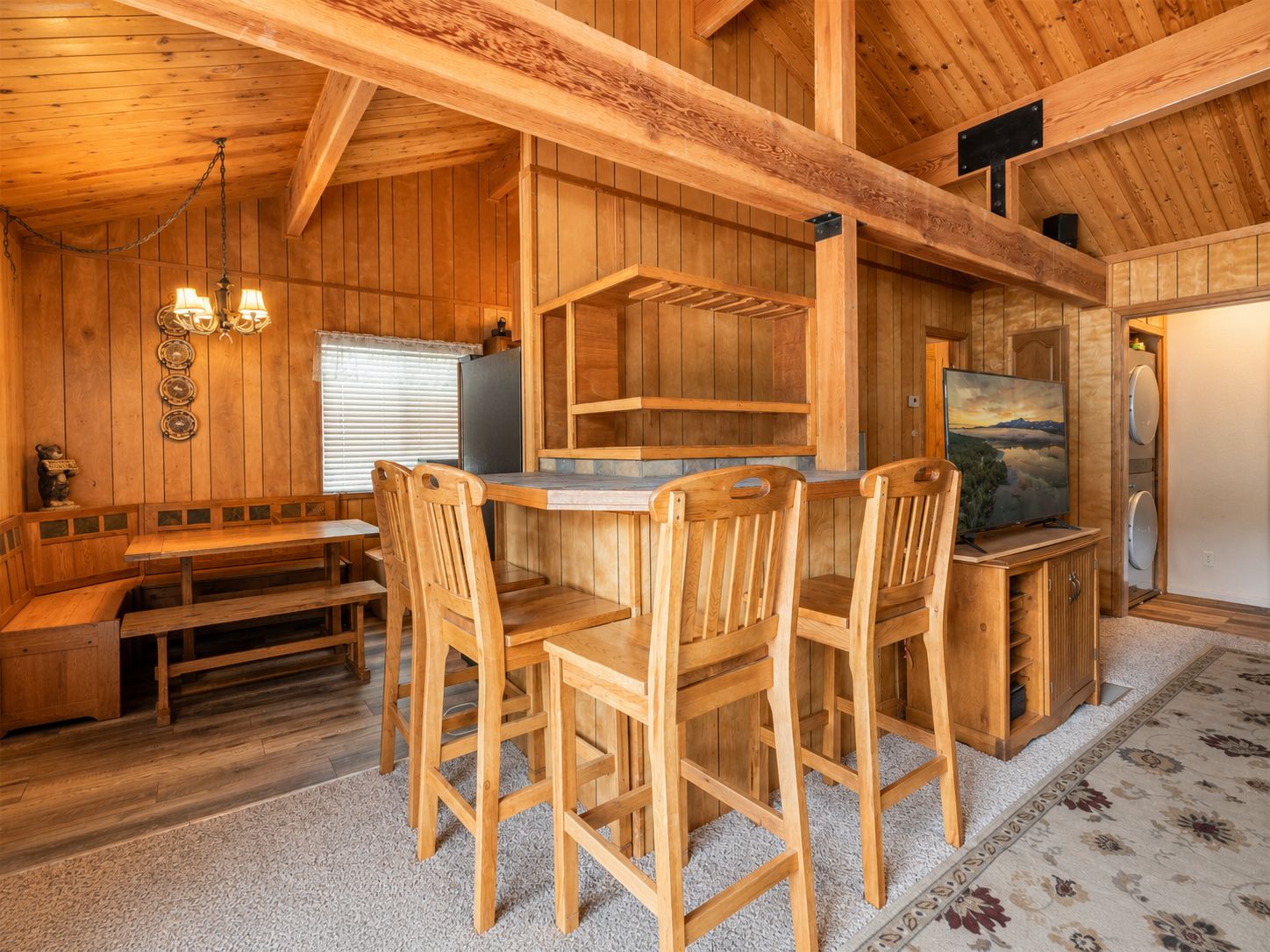 A wooden interior with a dining area, a bench, a television, and a refrigerator.