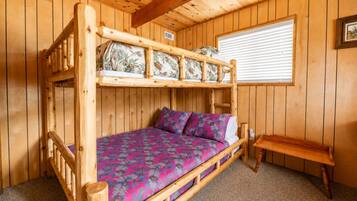 A bunk bed with a floral bedspread and pillows, a wooden bench, and a window with blinds.