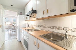 A modern kitchen with white cabinets, a stainless steel sink, and a built-in oven. - Sam65i Central 2 Bed Penthouse in Nueva Andalucia (Marbella)