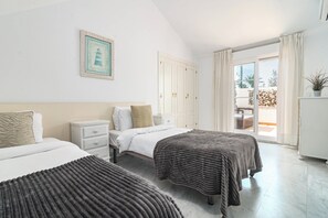 A hotel room with two beds, a nightstand, a wardrobe, and a balcony with a view. - Sam65i Central 2 Bed Penthouse in Nueva Andalucia (Marbella)