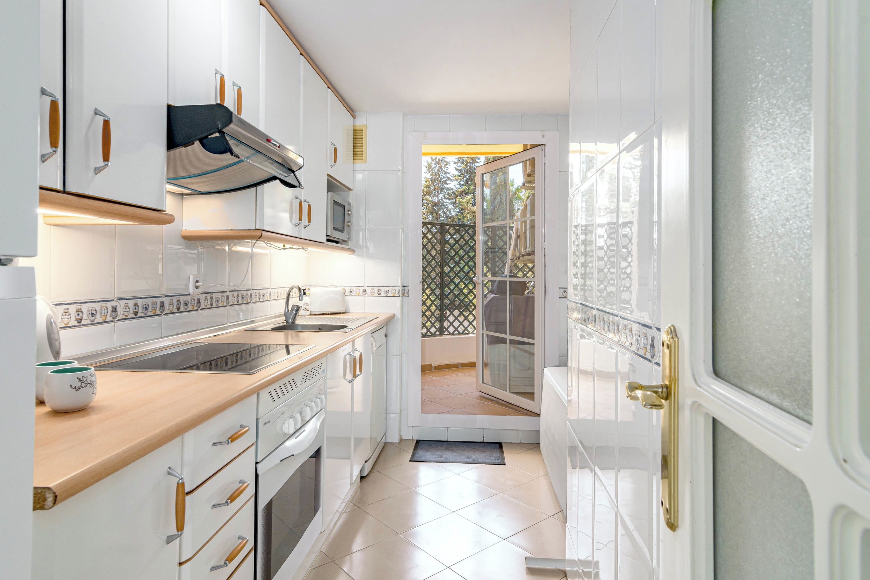 A modern kitchen with white cabinetry, a wooden countertop, and a view of the outdoors through a sliding glass door.