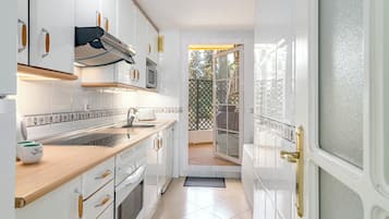 Une cuisine moderne avec des meubles blancs, un plan de travail en bois et une vue sur l’extérieur grâce à une porte-fenêtre coulissante.