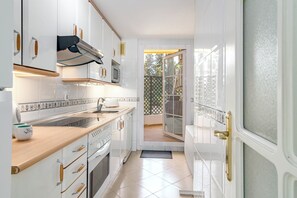A modern kitchen with white cabinetry, a wooden countertop, and a view of the outdoors through a sliding glass door. - Sam65i Central 2 Bed Penthouse in Nueva Andalucia (Marbella)