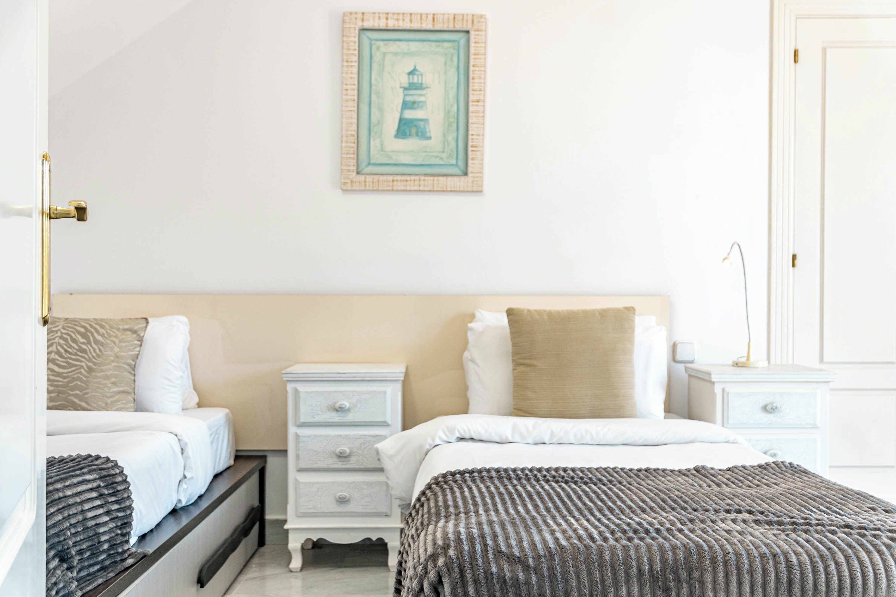 Une chambre d’hôtel avec un lit, des tables de chevet, une petite table et un tableau accroché au mur.