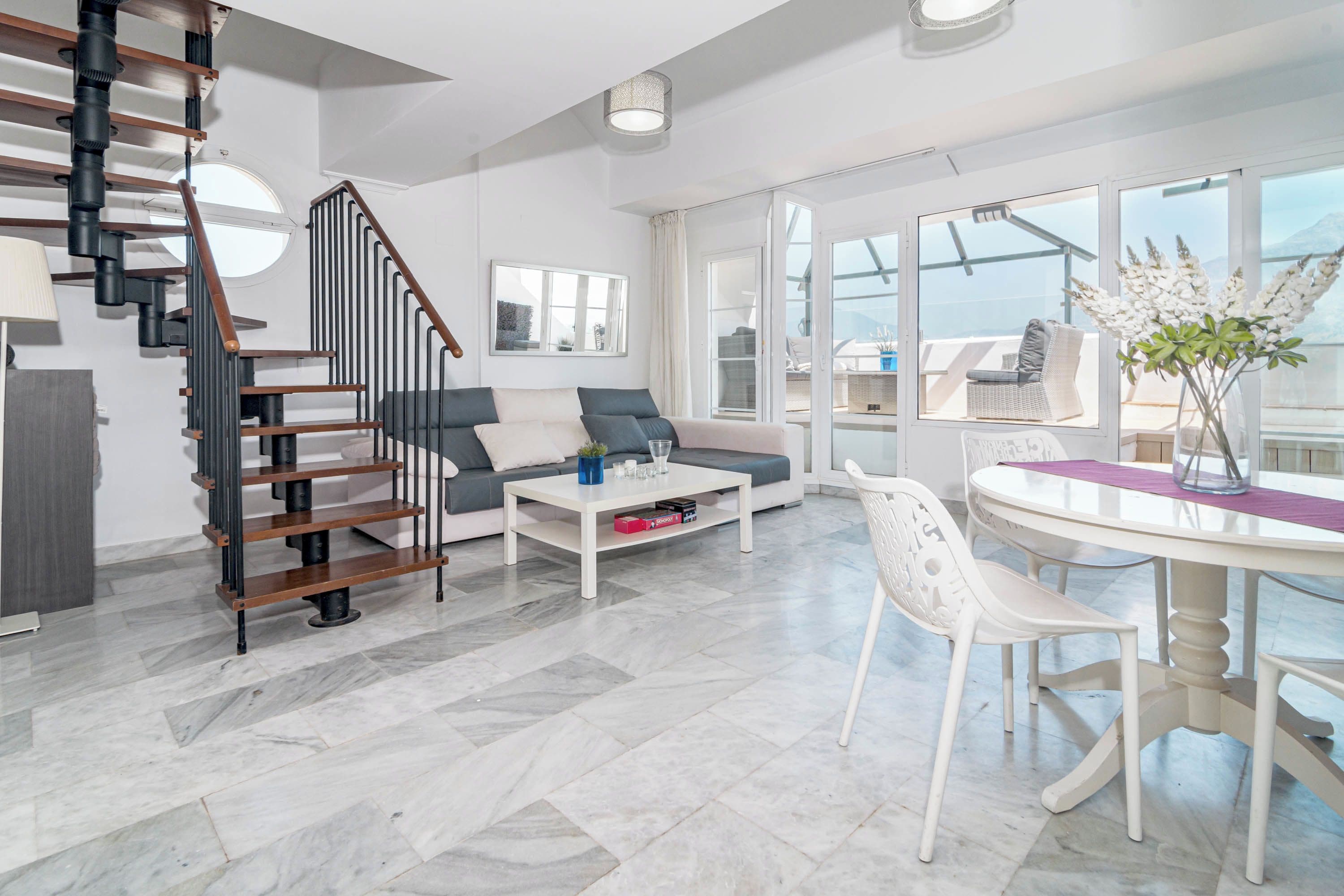 Un salon moderne avec un escalier, un canapé, une table basse et un coin repas doté d’une table en verre.
