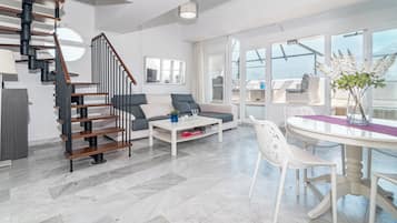 Un salon moderne avec un escalier, un canapé, une table basse et un coin repas doté d’une table en verre.