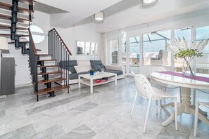 A modern living room with a staircase, a sofa, a coffee table, and a dining area with a glass table. - Sam65i Central 2 Bed Penthouse in Nueva Andalucia (Marbella)