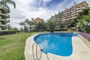 A swimming pool with a metal ladder, surrounded by a well-maintained lawn and palm trees. - Sam65i Central 2 Bed Penthouse in Nueva Andalucia (Marbella)