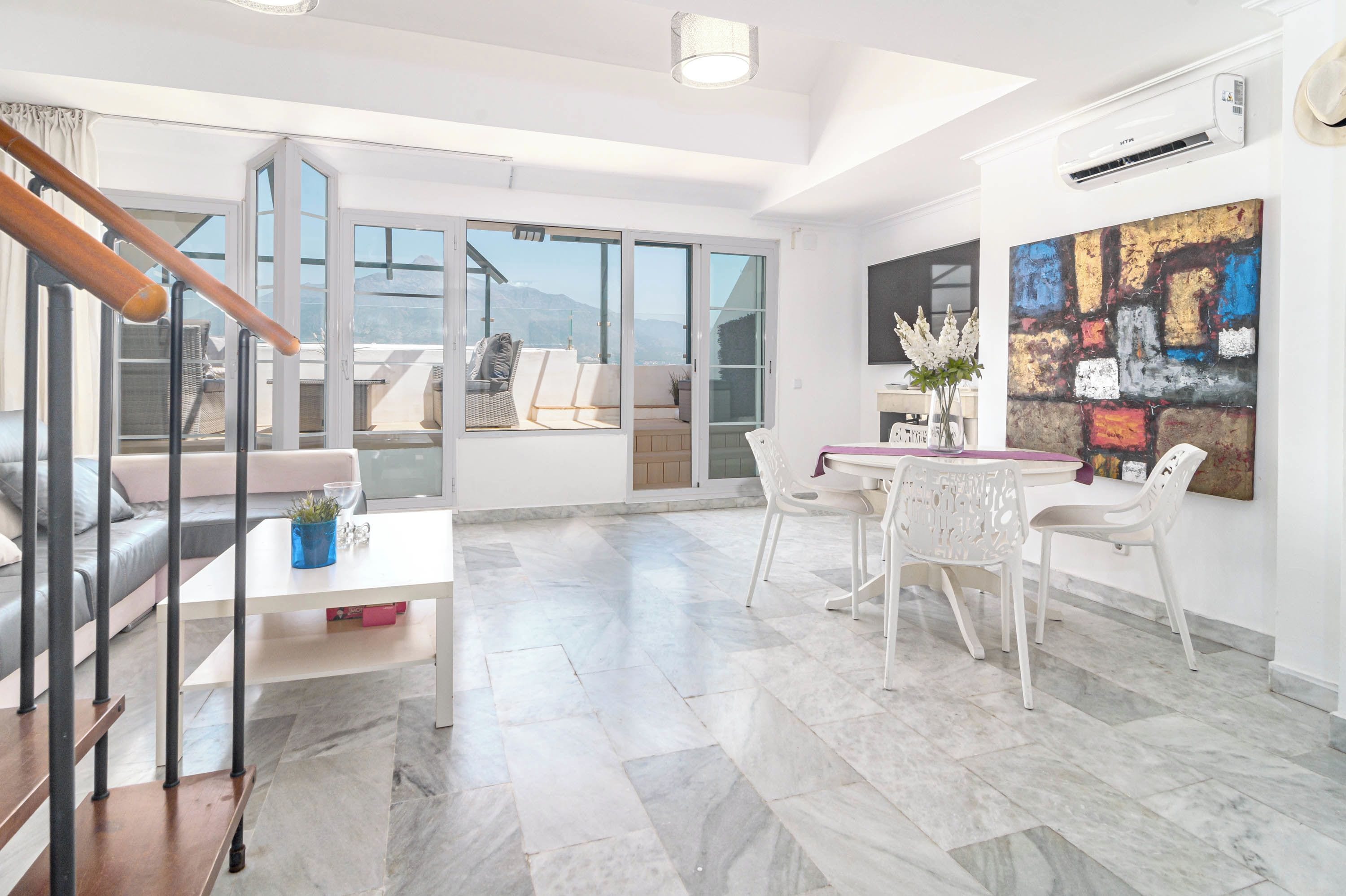 A spacious living area with a balcony, a dining table with chairs, and a large abstract painting on the wall.