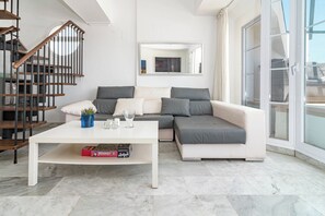 Un salón moderno con un sofá blanco, una mesa de centro y una escalera con barandillas de madera.