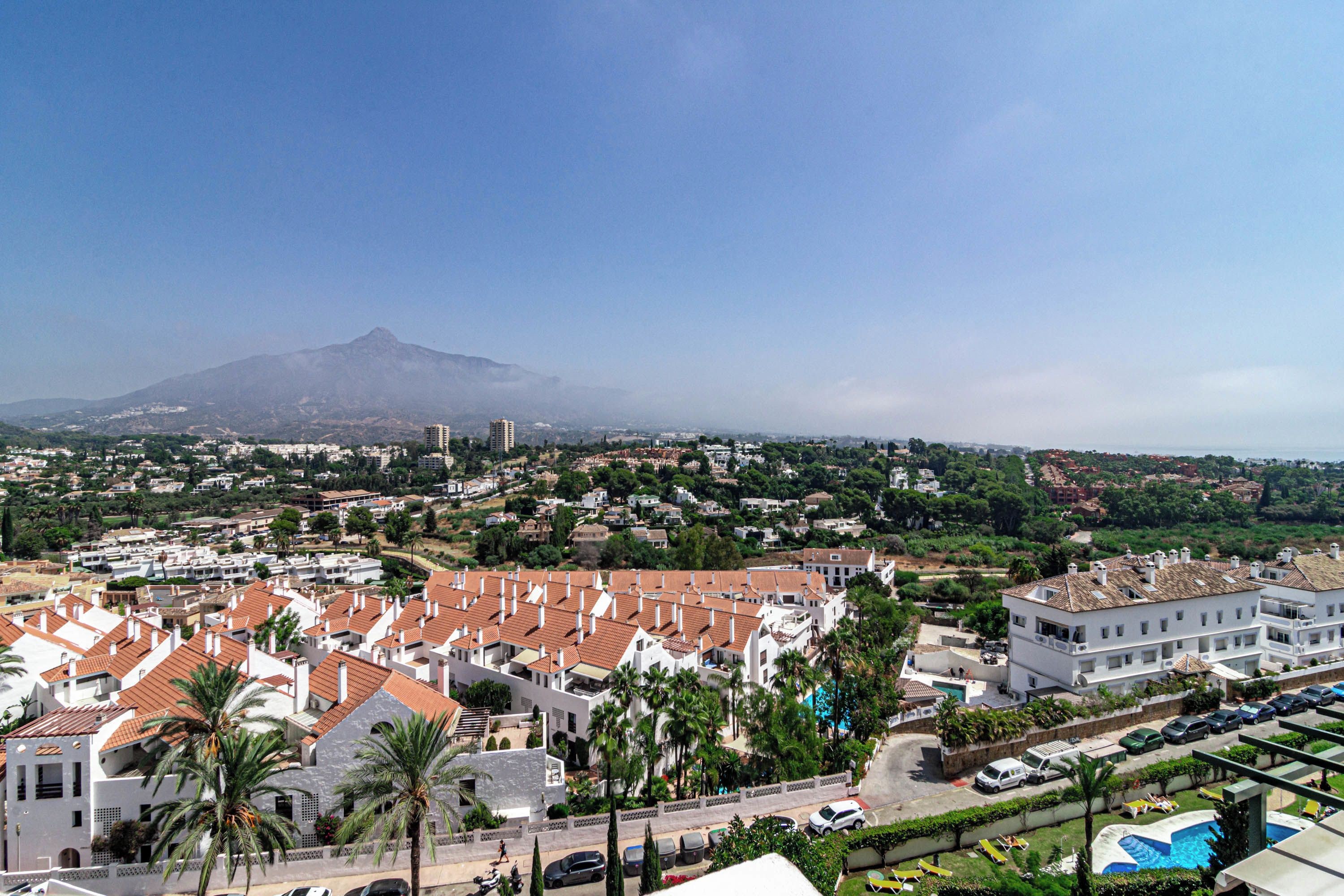 A residential area with white buildings, a mountain in the background, and a clear sky.