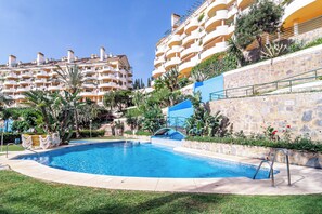 Una piscina rodeada por un muro de piedra, con un cielo azul y un edificio de varios pisos al fondo.