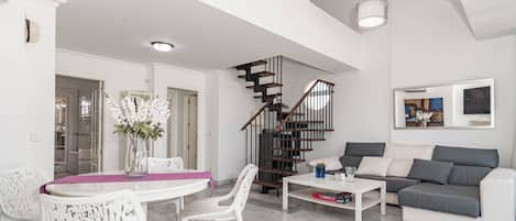 Ein modernes Wohnzimmer mit einem weißen Sofa, einem Esstisch mit Stühlen, einer Treppe und einer Deckenleuchte.