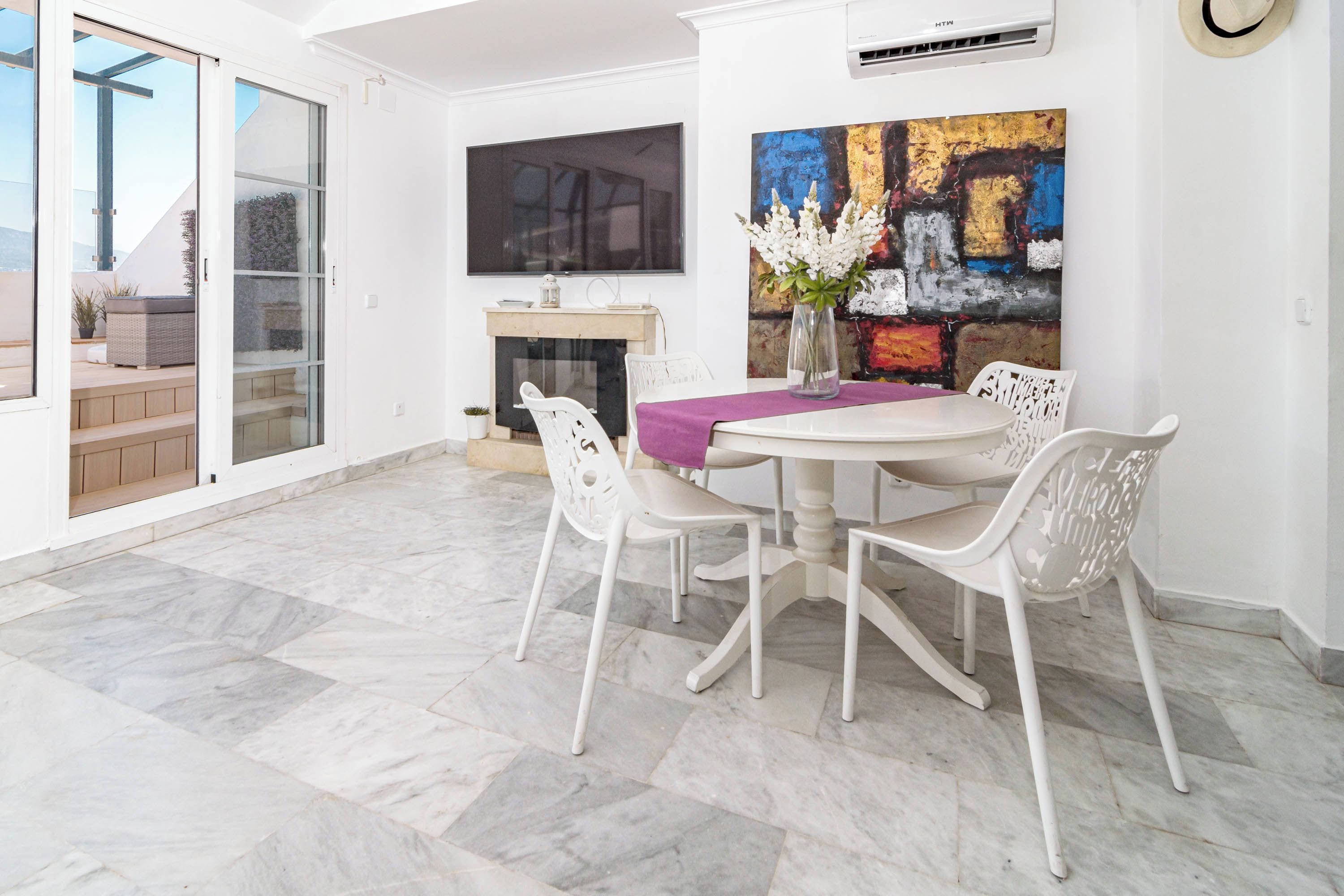 A dining area with a round table, white chairs, a fireplace, and a large abstract painting.
