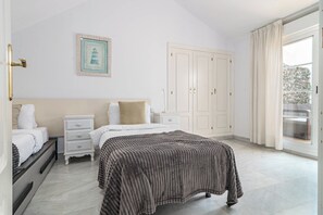 Un dormitorio con cama, mesita de noche, cómoda, armario y ventana con cortinas.