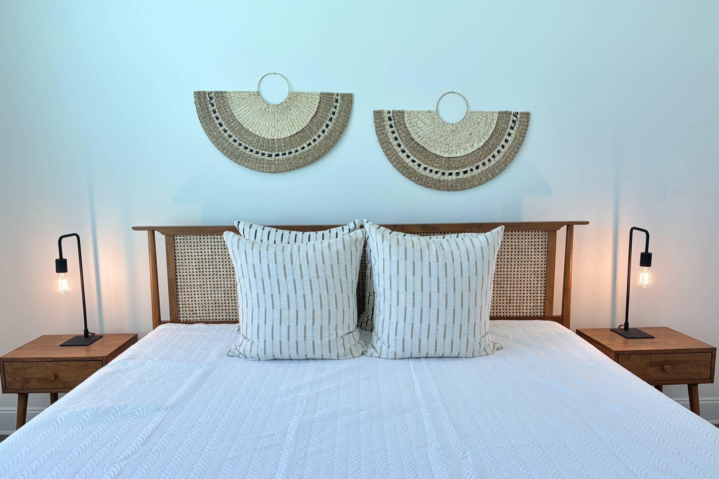 Un lit avec un matelas matelassé blanc, deux oreillers, une tête de lit en bois et deux lampes de chevet.