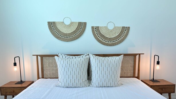 A bed with a white quilted mattress, two pillows, a wooden headboard, and two bedside lamps. - Private Beach Access, Beautiful Ocean Views, Balcony, Brand New Furnishings, $300 in Free Tickets! (St. Augustine)