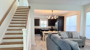 A modern kitchen with dark cabinets, a stainless steel refrigerator, and a dining area with a gray sofa and striped pillows. - Private Beach Access, Beautiful Ocean Views, Balcony, Brand New Furnishings, $300 in Free Tickets! (St. Augustine)