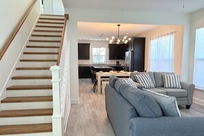 A modern kitchen with dark cabinets, a stainless steel refrigerator, and a dining area with a gray sofa and striped pillows. - Private Beach Access, Beautiful Ocean Views, Balcony, Brand New Furnishings, $300 in Free Tickets! (St. Augustine)