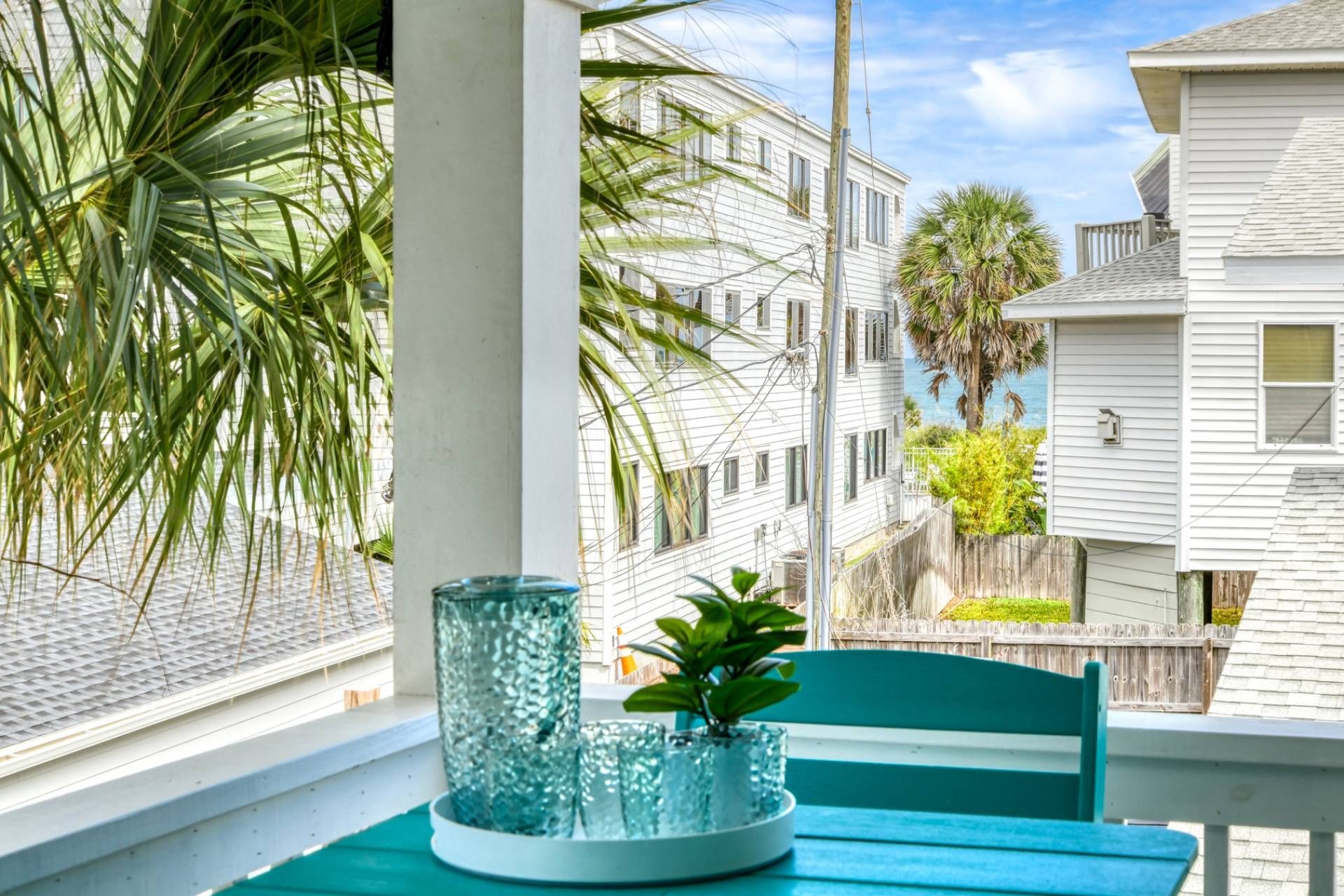 A view from a window with a table and chairs, a glass vase with plants, and a building with multiple windows and balconies.
