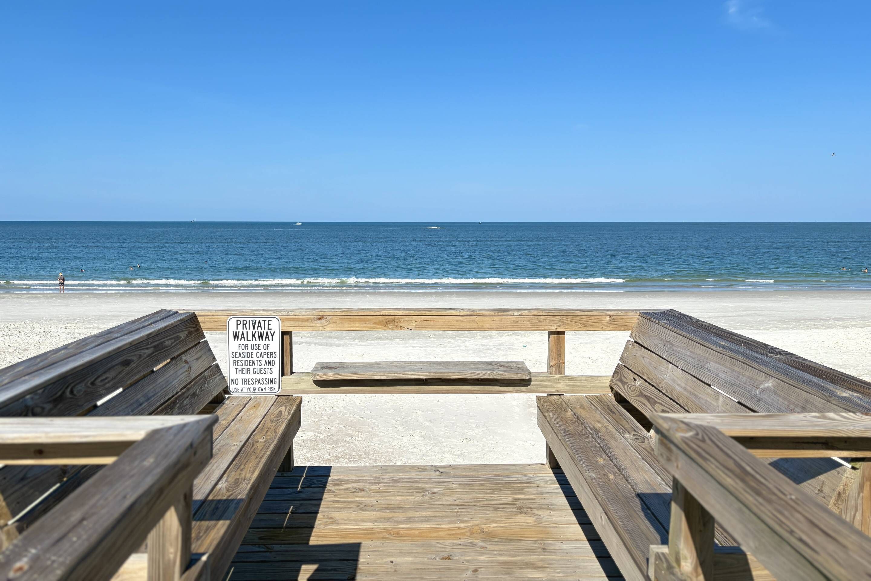 Une promenade en bois mène à une plage, et une pancarte indique qu’il s’agit d’un sentier privé réservé aux résidents et à leurs invités.