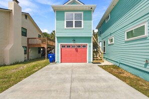 A two-story house with a red garage door, a small balcony, and a wooden staircase leading to the upper level.