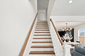A staircase with wooden steps and white railings leading to a room with a dining table and chairs.