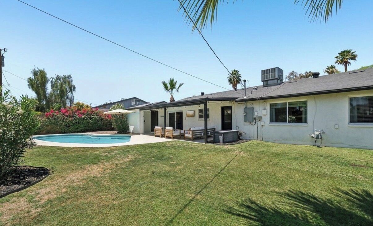 A residential property with a swimming pool, a covered patio, and a lawn.