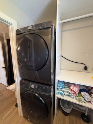 Un appareil compact combinant lave-linge et sèche-linge, doté d’un panneau de commande, d’un câble d’alimentation et d’une étagère où sont pliées des serviettes.