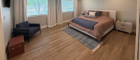 Un dormitorio con cama, una silla, una mesita de noche, ventilador de techo y ventana con persianas.