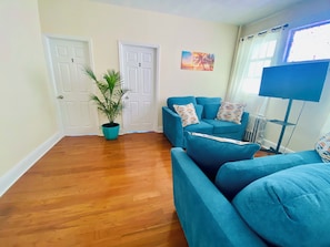 A living room with a blue sofa set, a potted plant, and a painting on the wall. - Charming 3-bedroom apartment with AC in Irvington (Irvington)