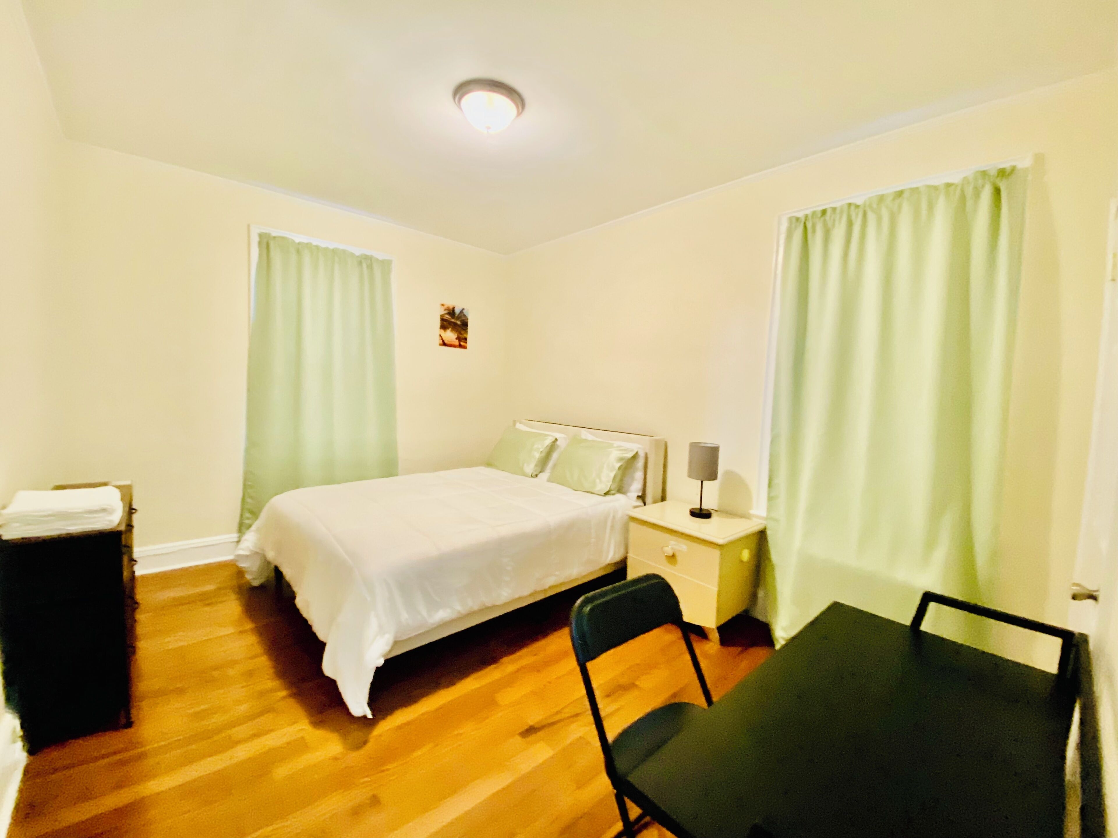 A hotel room with a bed, bedside table, lamp, chair, and a small table.