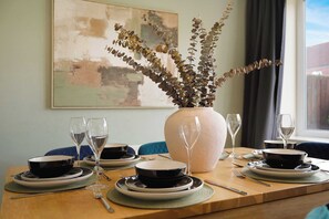 A dining table set with plates, bowls, and wine glasses, with a vase of dried foliage in the center. - Modern 4BR Stay Driveway Parking By Stay With Us (Middlesbrough)