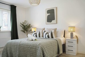Una camera da letto con un letto, lampade sui comodini, una pianta e un quadro appeso al muro.
