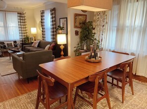 A dining area with a wooden table and chairs, a sofa, a lamp, and a plant. - Charming Dundee Artist's Bungalow, Walkable to Shops, Restaurants, Memorial Park (Omaha)
