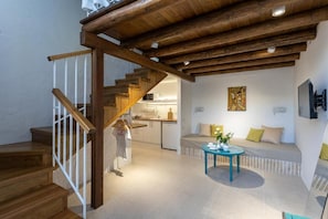 A modern interior with a wooden staircase, a kitchen in the background, and a seating area with a table.