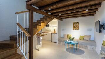 Ein modernes Interieur mit einer Holztreppe, einer Küchenzeile, einer Sitzecke mit Sofa und Tisch sowie einem Gemälde an der Wand.