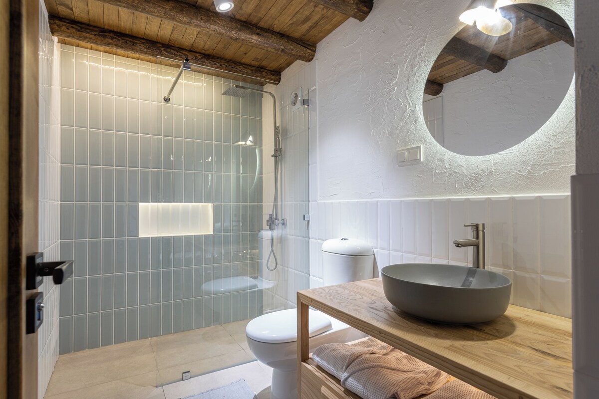 A modern bathroom with a glass shower enclosure, a toilet, a sink with a large basin, and a wooden vanity.