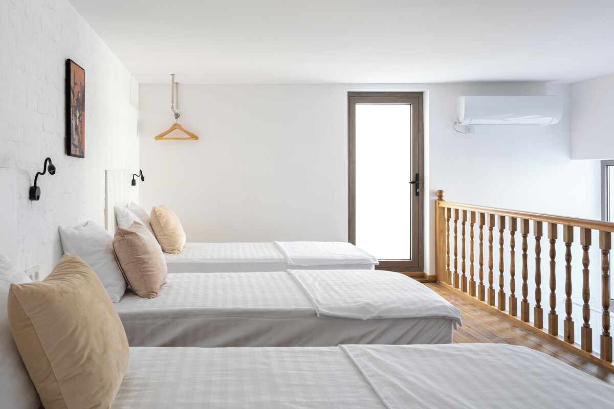 A hotel room with two beds, a wooden railing, a white wall with a picture, and a door.