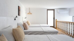 Una habitación de hotel con dos camas, una barandilla de madera, una pared blanca con un cuadro y una puerta.