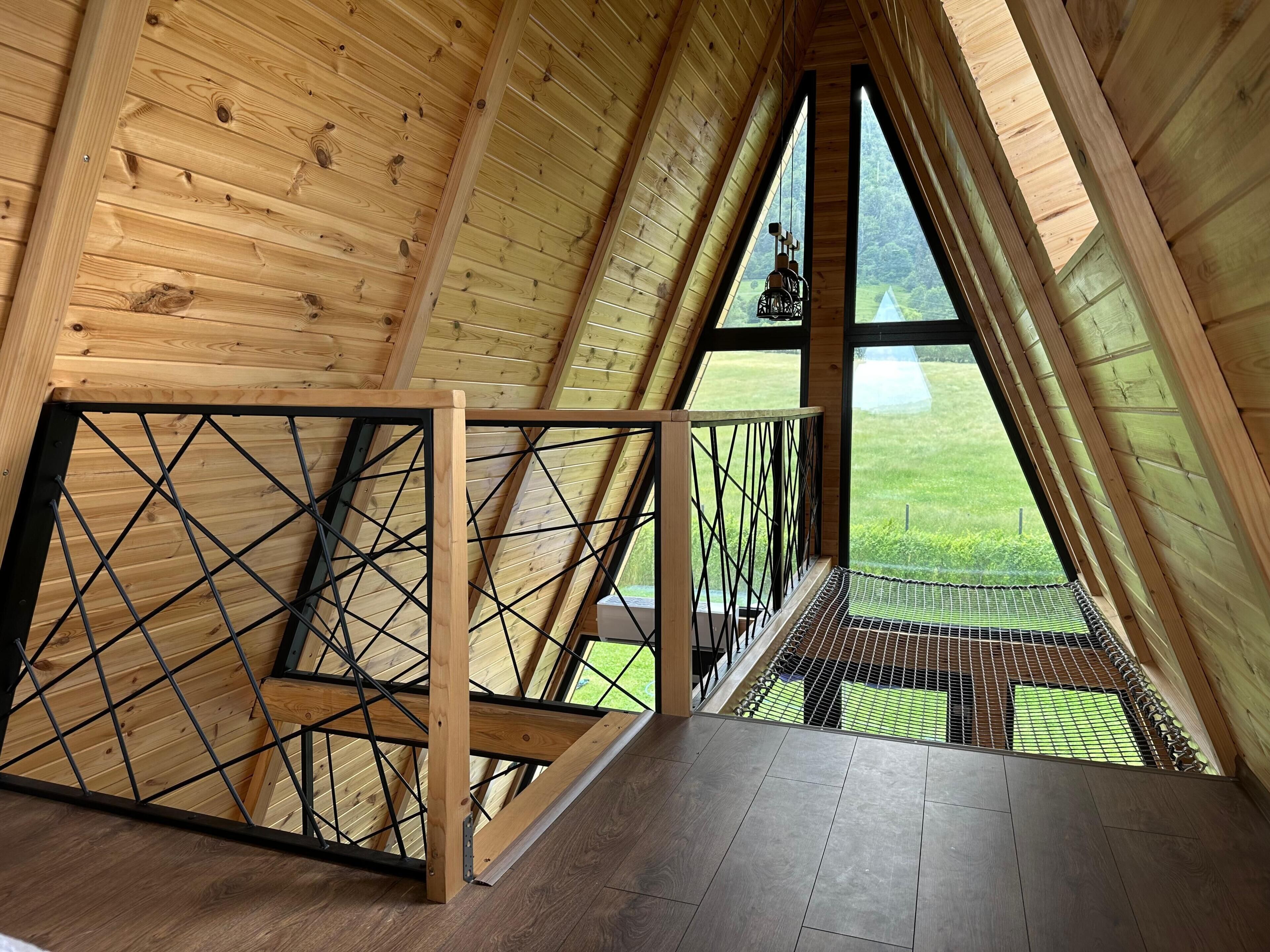Une pièce mansardée en bois, avec un plafond en pente, un escalier en métal et une vue sur un paysage verdoyant.