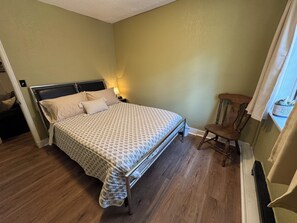 A bedroom with a bed, bedside table, lamp, chair, and a window with curtains. - 3-bedroom cottage in peaceful Colorado Springs with AC (Colorado Springs)