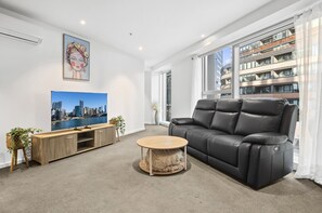 Een moderne woonkamer met een zwarte leren bank, een houten salontafel, een flatscreen-televisie en een stadsgezicht schilderij.