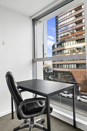 Ein moderner Bürostuhl und Schreibtisch vor einem großen Fenster mit Blick auf eine Skyline.