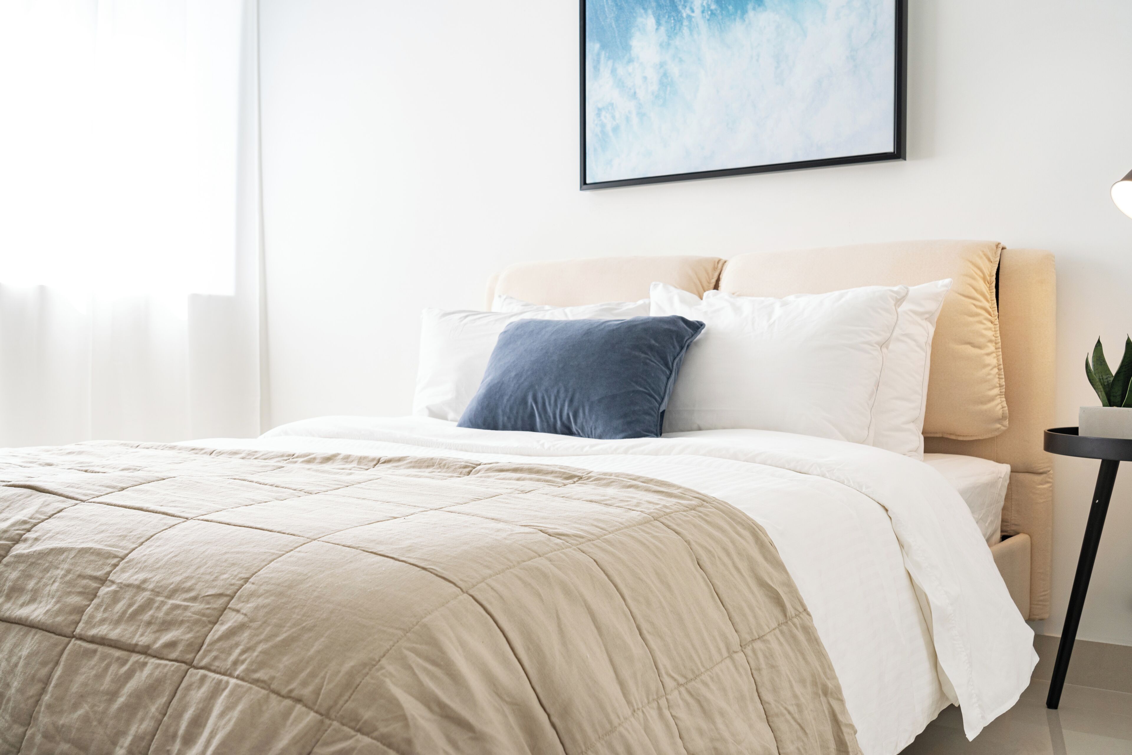 Una cama bien hecha con un edredón color beige, una almohada blanca y una almohada azul.