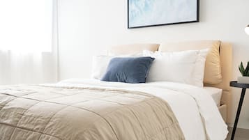 Una cama bien hecha con un edredón color beige, una almohada blanca y una almohada azul.