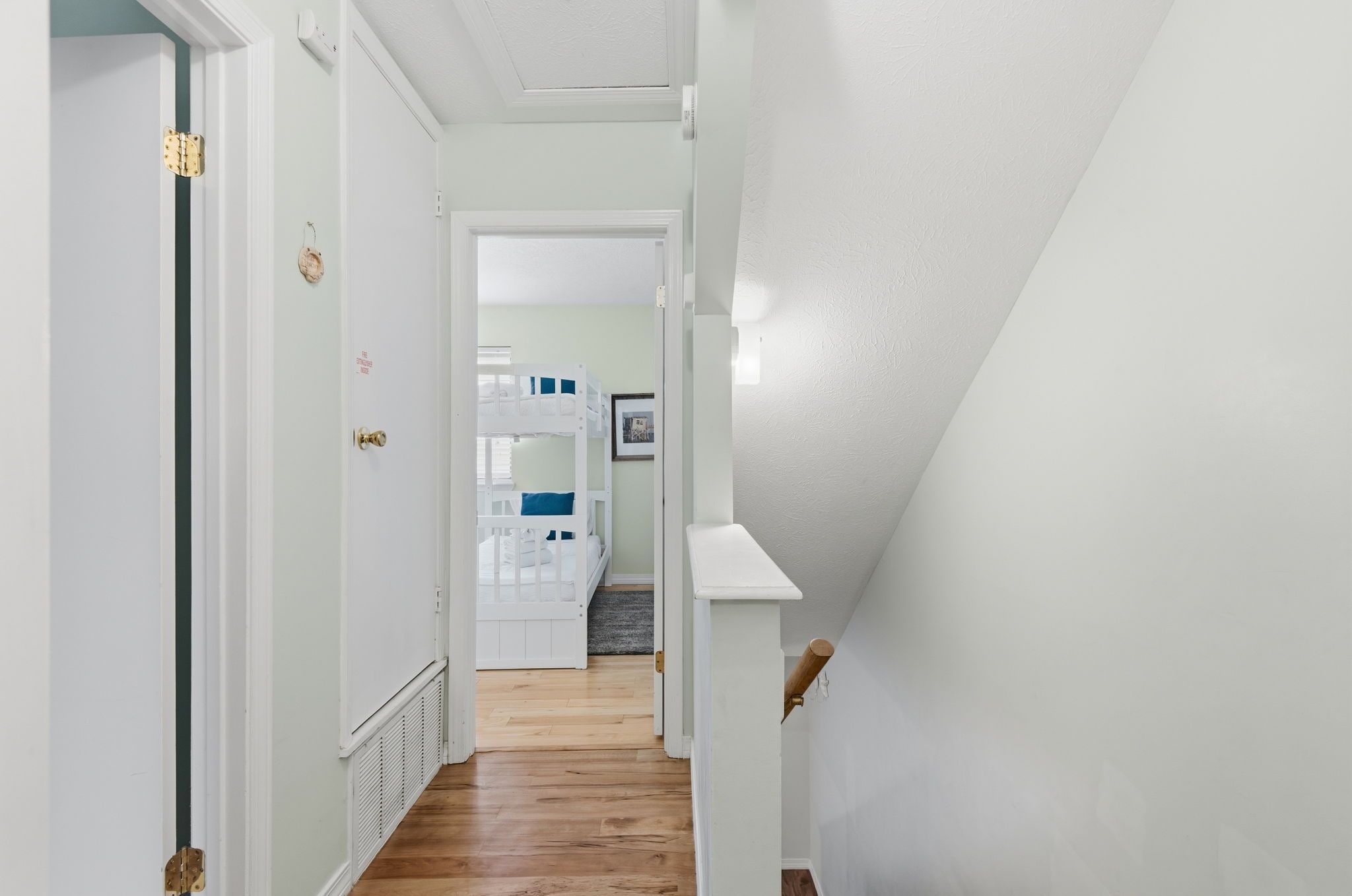 A hallway with a wooden floor leading to a room with bunk beds.