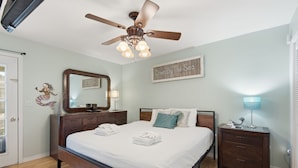 A bedroom with a bed, a ceiling fan, a nightstand, a lamp, a mirror, and a sign on the wall.