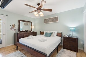 A bedroom with a bed, a ceiling fan, a nightstand, a lamp, a mirror, and a sign on the wall.